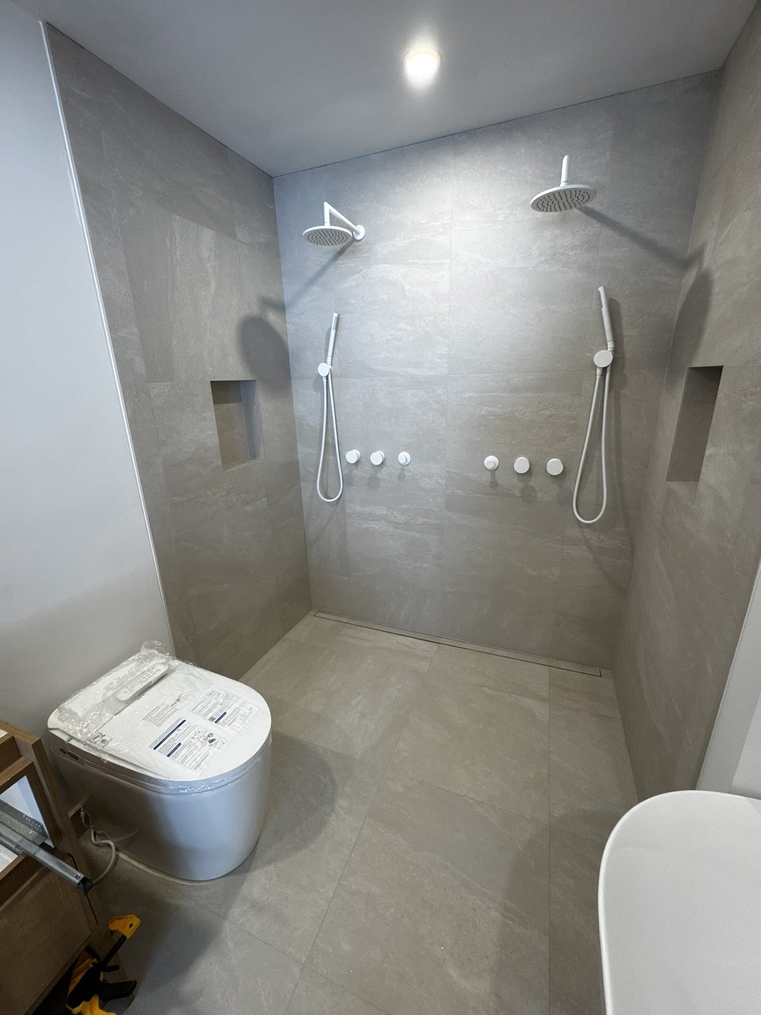 Douche à deux postes et toilette dans une salle de bain aux tons clairs